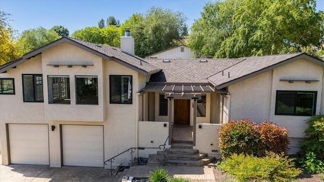 split level home featuring an attached garage, a chimney, a shingled roof, and stucco siding