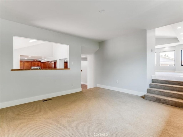 unfurnished living room with carpet floors, baseboards, visible vents, and stairway