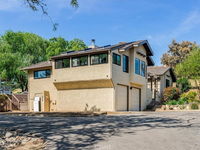exterior space featuring a garage, stucco siding, a chimney, roof mounted solar panels, and driveway