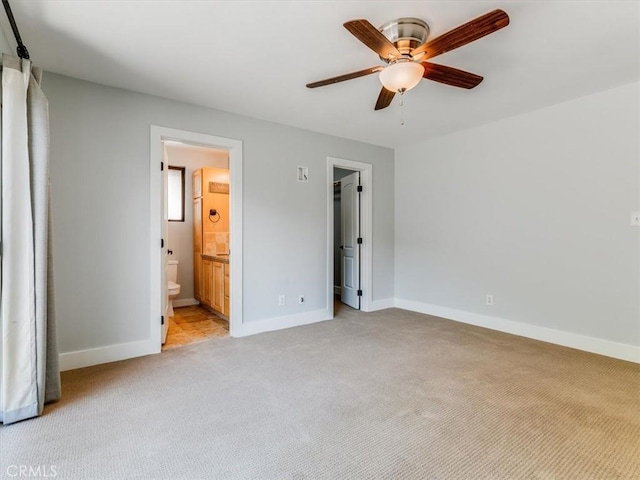 unfurnished bedroom with baseboards, ensuite bathroom, light carpet, and ceiling fan