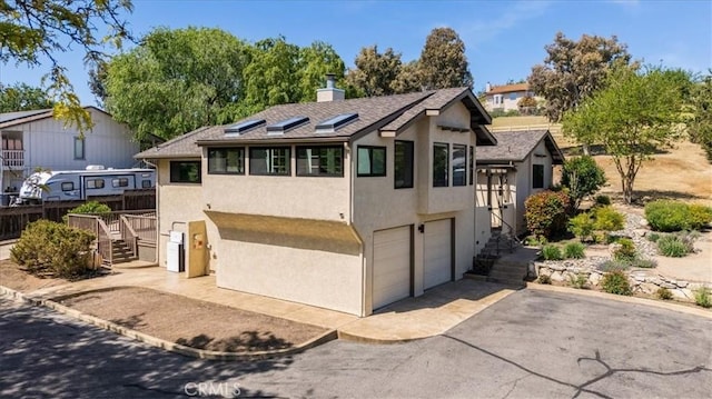 exterior space with stucco siding, a chimney, stairs, an attached garage, and driveway