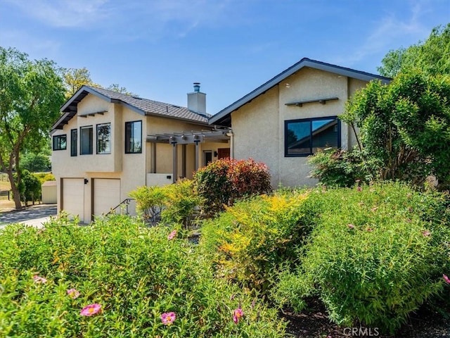 view of front facade featuring concrete driveway, an attached garage, a chimney, and stucco siding