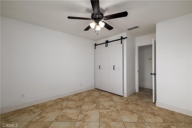 unfurnished bedroom featuring baseboards, visible vents, a barn door, and ceiling fan
