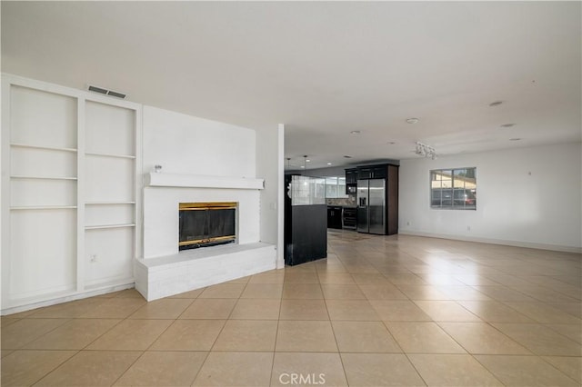 unfurnished living room with visible vents, built in shelves, light tile patterned floors, and a fireplace