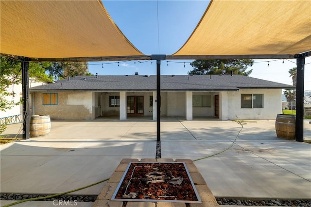 back of house with roof with shingles, a patio area, and stucco siding
