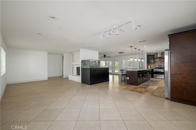 kitchen with wall chimney range hood, backsplash, a ceiling fan, appliances with stainless steel finishes, and open floor plan