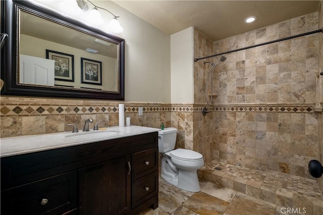 full bathroom with tile walls, toilet, vanity, and a tile shower