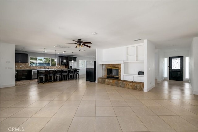 unfurnished living room featuring light tile patterned flooring, a ceiling fan, visible vents, and baseboards