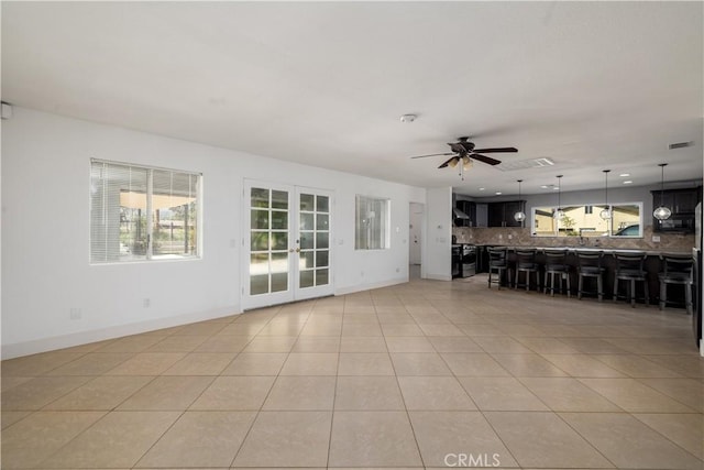 unfurnished living room with visible vents, light tile patterned flooring, baseboards, french doors, and a ceiling fan
