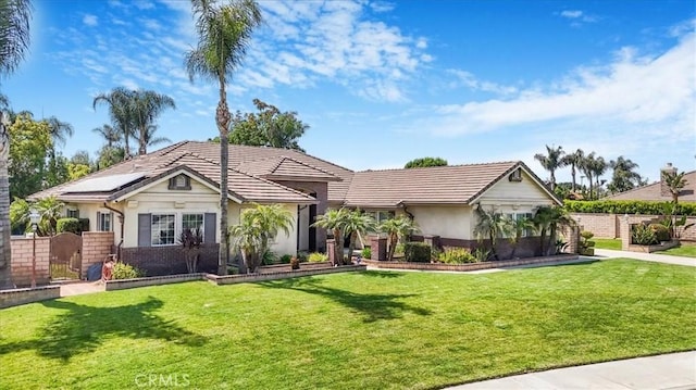 ranch-style home with a tiled roof, a front yard, fence, roof mounted solar panels, and stucco siding