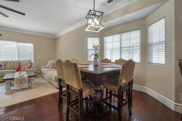 dining space with dark wood-style flooring, ceiling fan with notable chandelier, baseboards, visible vents, and ornamental molding
