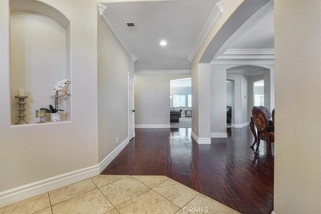 corridor with visible vents, arched walkways, hardwood / wood-style flooring, baseboards, and ornamental molding