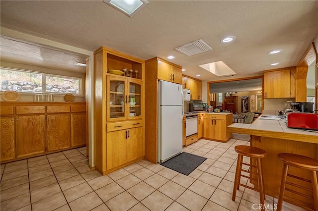 kitchen with white appliances, a peninsula, tile countertops, light tile patterned floors, and visible vents