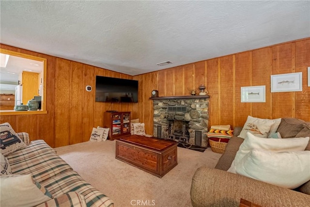 living area featuring visible vents, wood walls, carpet floors, a stone fireplace, and a textured ceiling