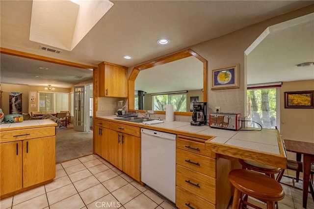 kitchen with tile countertops, dishwasher, a sink, a peninsula, and open floor plan