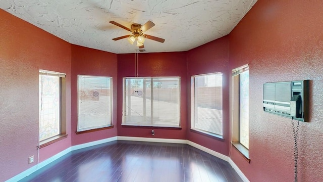 spare room featuring a textured wall, wood-type flooring, ceiling fan, and a wealth of natural light