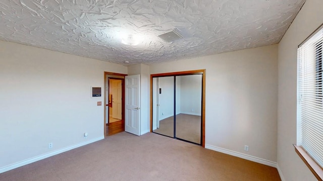 unfurnished bedroom with a textured ceiling, visible vents, baseboards, a closet, and carpet flooring