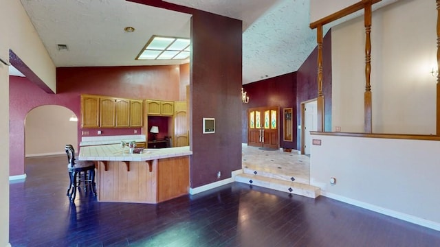 kitchen with dark wood-style flooring, tile counters, arched walkways, baseboards, and visible vents