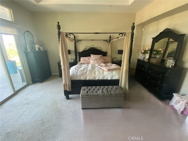 carpeted bedroom with access to outside and a tray ceiling