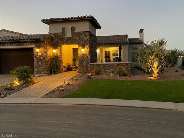 mediterranean / spanish home featuring a front yard, stone siding, stucco siding, a tiled roof, and an attached garage