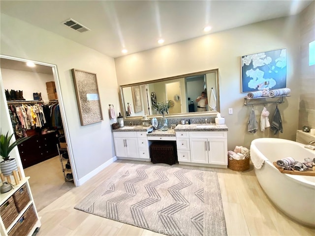 bathroom featuring vanity, a freestanding tub, wood finished floors, a spacious closet, and visible vents