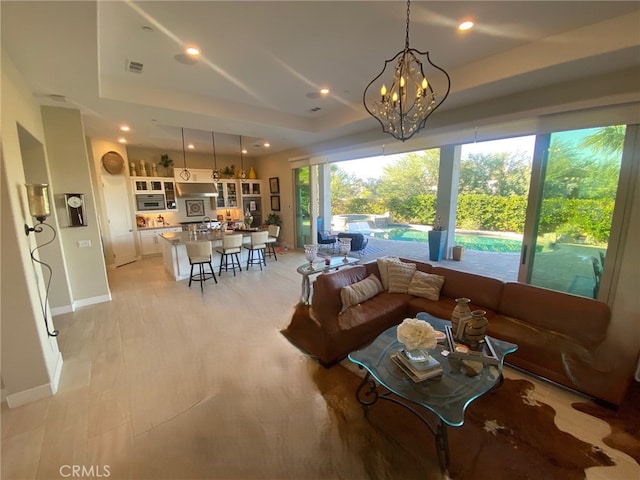 living area featuring a raised ceiling, baseboards, recessed lighting, and a notable chandelier