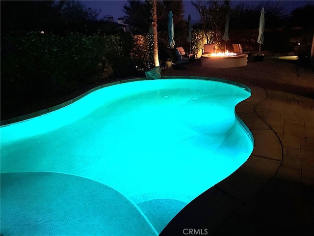 pool at night with a patio, an outdoor pool, and an outdoor fire pit