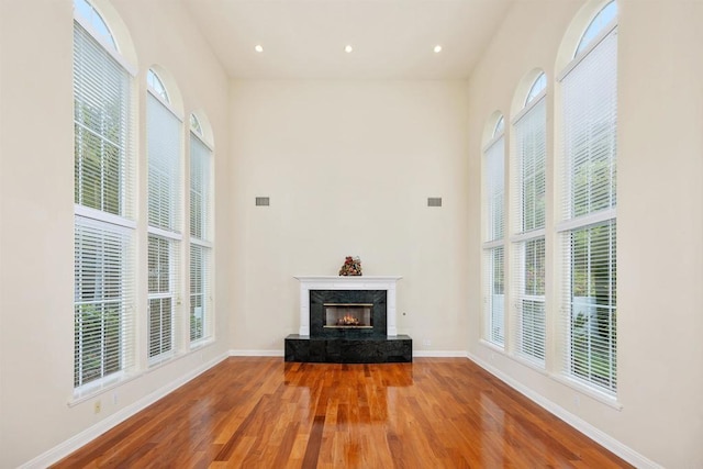 unfurnished living room featuring a wealth of natural light, wood finished floors, and a high end fireplace