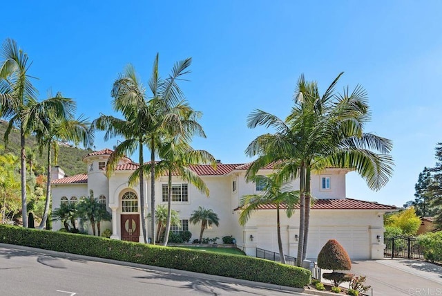 mediterranean / spanish-style home featuring fence, stucco siding, an attached garage, and driveway