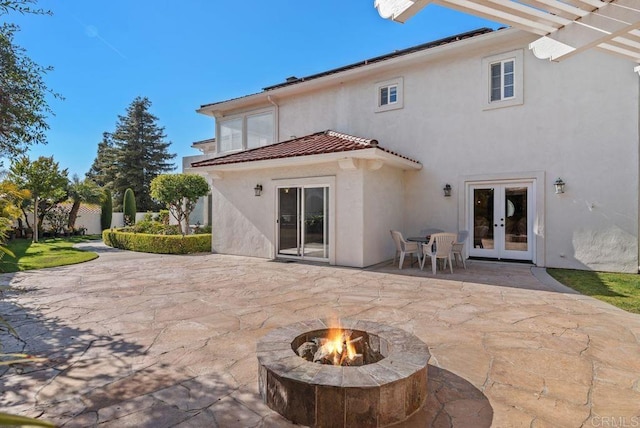 rear view of property featuring stucco siding, french doors, a patio, a tiled roof, and a fire pit