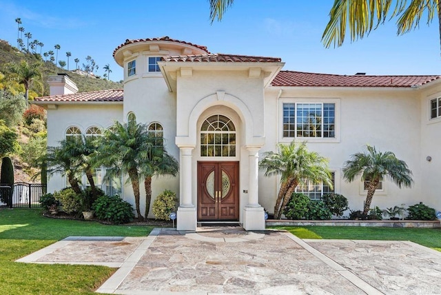 view of front of house featuring a tiled roof, a chimney, fence, a front lawn, and stucco siding