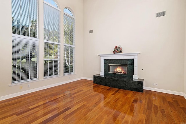 unfurnished living room featuring baseboards, visible vents, wood finished floors, and a high end fireplace