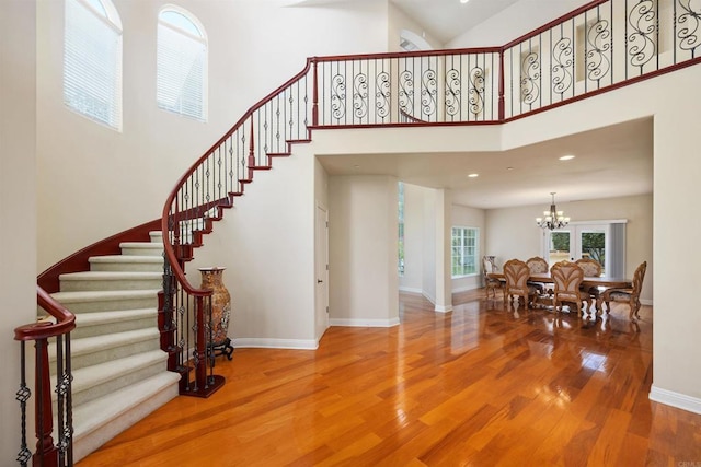 foyer featuring wood finished floors, baseboards, a high ceiling, stairway, and a chandelier