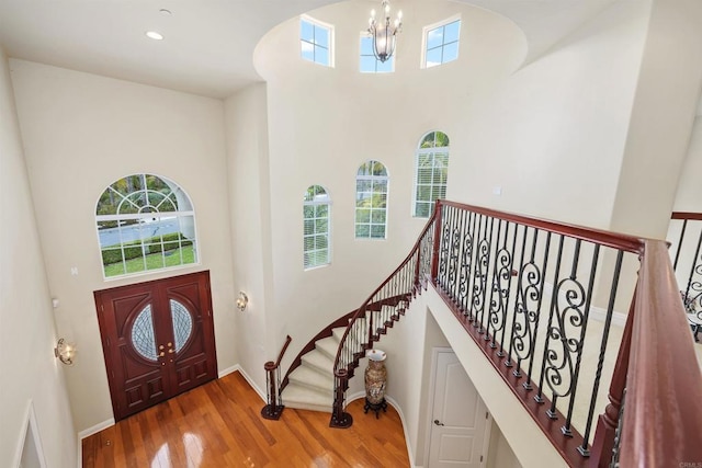 foyer featuring baseboards, an inviting chandelier, wood finished floors, and a towering ceiling