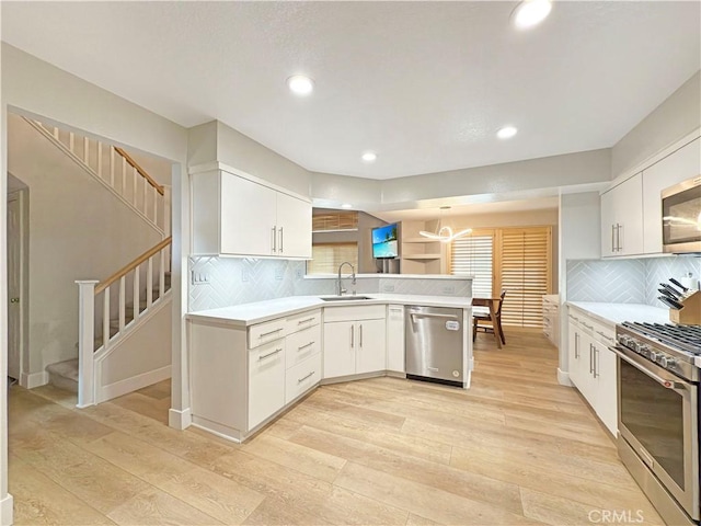 kitchen with appliances with stainless steel finishes, a sink, light wood finished floors, light countertops, and a peninsula