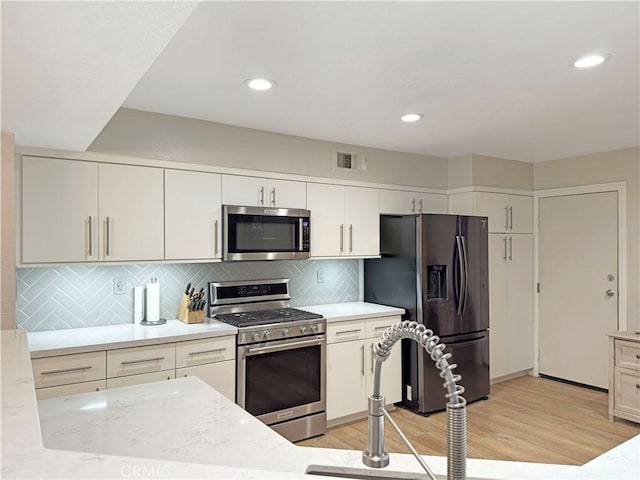 kitchen featuring decorative backsplash, visible vents, appliances with stainless steel finishes, light wood-type flooring, and white cabinets