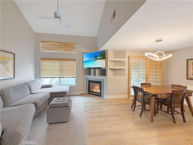 living room with vaulted ceiling, a tile fireplace, baseboards, ceiling fan with notable chandelier, and light wood finished floors
