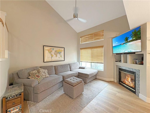 living area featuring a ceiling fan, a tile fireplace, high vaulted ceiling, baseboards, and light wood finished floors