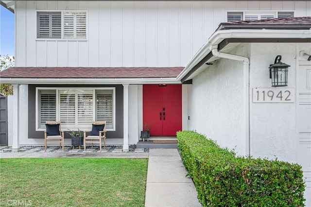 doorway to property featuring a porch, roof with shingles, and a lawn