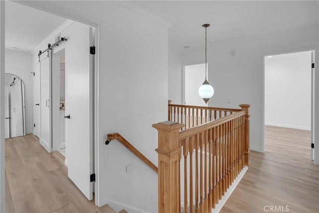 hallway with crown molding, light wood-style floors, baseboards, a barn door, and an upstairs landing