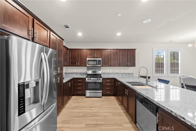 kitchen featuring light wood-type flooring, a sink, light stone counters, and stainless steel appliances