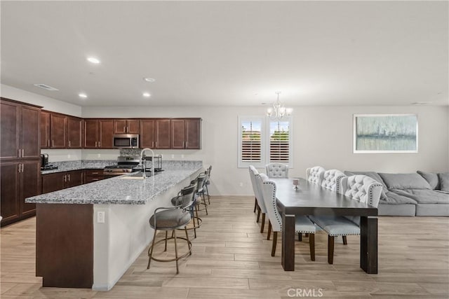 kitchen featuring light wood-style floors, a kitchen bar, a sink, an inviting chandelier, and stainless steel appliances