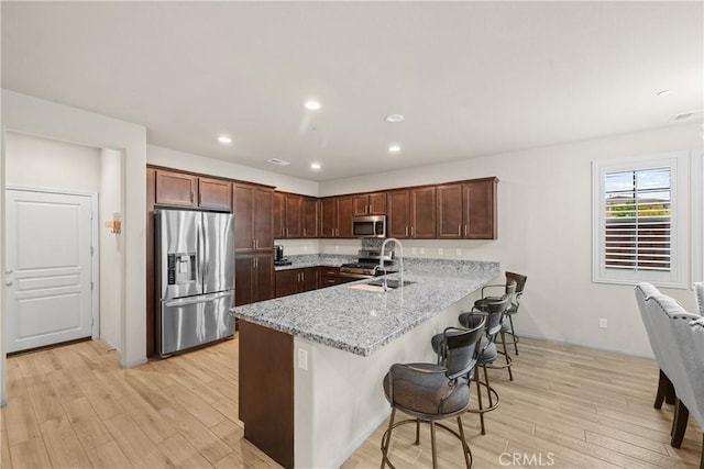 kitchen featuring a peninsula, appliances with stainless steel finishes, a sink, and light wood-style flooring