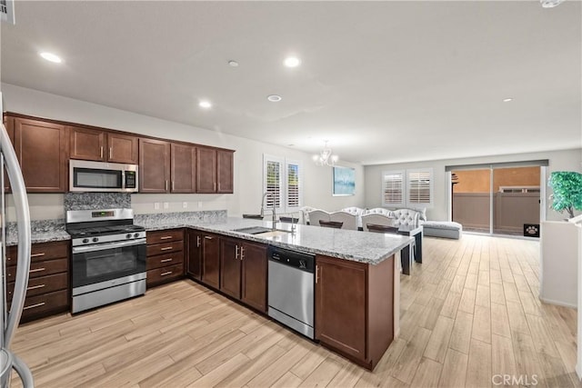 kitchen with light wood-style floors, a sink, a peninsula, an inviting chandelier, and stainless steel appliances
