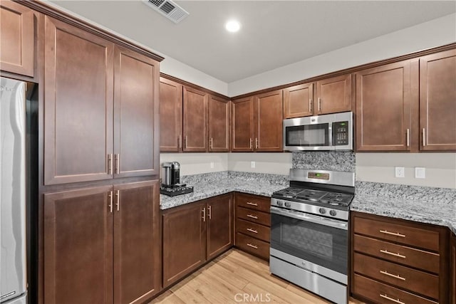 kitchen featuring visible vents, recessed lighting, light stone counters, light wood finished floors, and appliances with stainless steel finishes