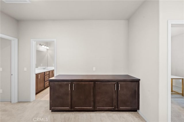 corridor featuring light colored carpet, a sink, and baseboards