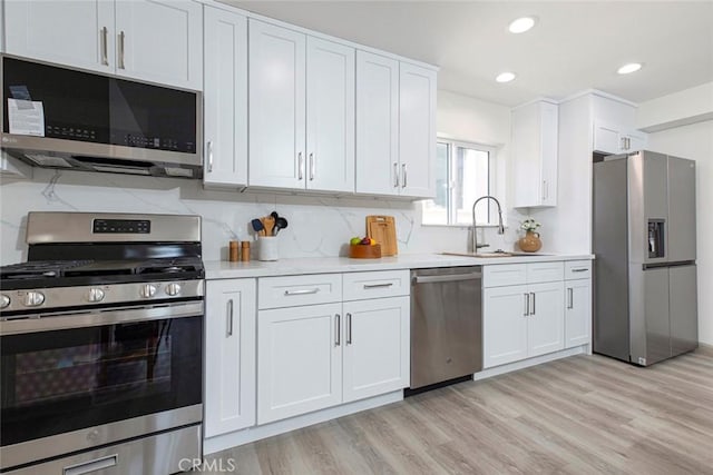 kitchen with white cabinets, appliances with stainless steel finishes, a sink, light wood-style floors, and light countertops