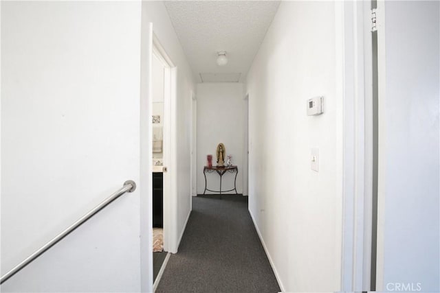 corridor with an upstairs landing, dark carpet, baseboards, and a textured ceiling