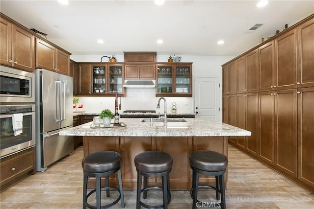 kitchen with light wood-style flooring, a breakfast bar area, under cabinet range hood, and stainless steel appliances