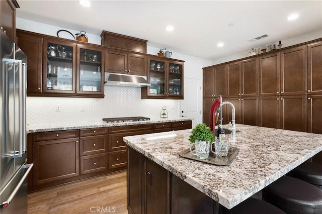 kitchen with stainless steel appliances, light wood-type flooring, tasteful backsplash, under cabinet range hood, and visible vents